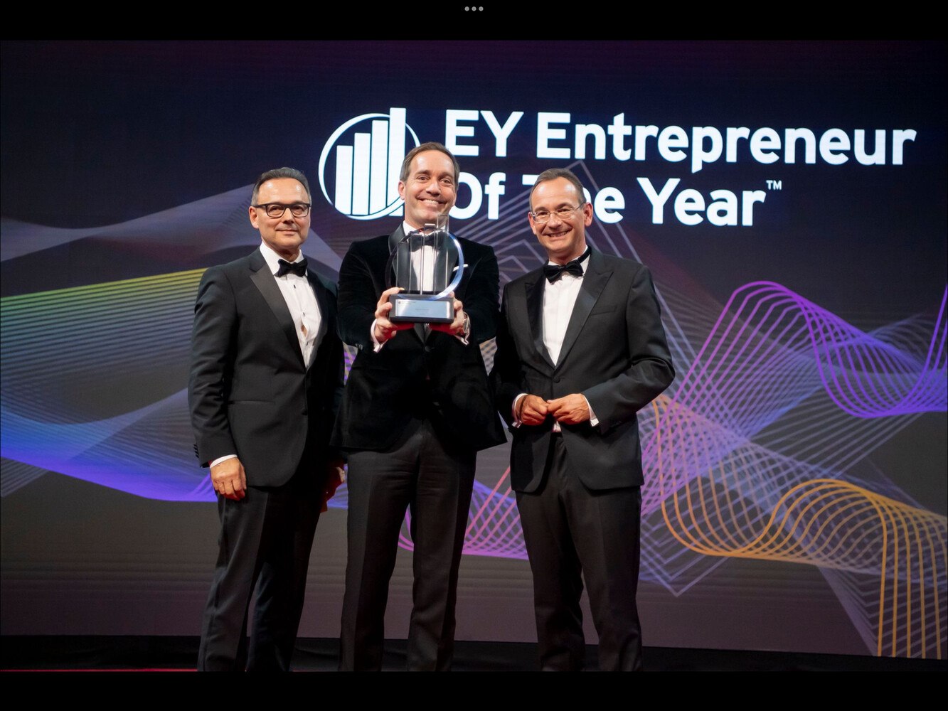 drei Männer im Anzug vor einem Plakat der Auszeichnung, Kröswang hält Preis