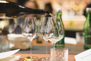 Nahaufnahme von Gläsern: Jemand schenkt gerade Weißwein ein.