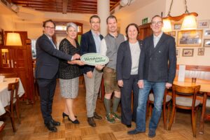 Eine Gruppe an Menschen seht in einem Wirtshaus und posiert für ein Pressefoto.