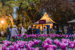 Besucher*innen stellen sich in einer Schlange an. Im Vordergrund blühen Tulpen.