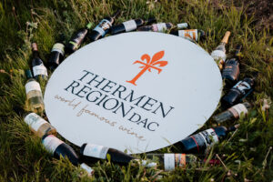 Weinflaschen sind im Kreis in der Wiese auggelegt. In der Mitte ist das Logo der Thermenregion DAC zu sehen.