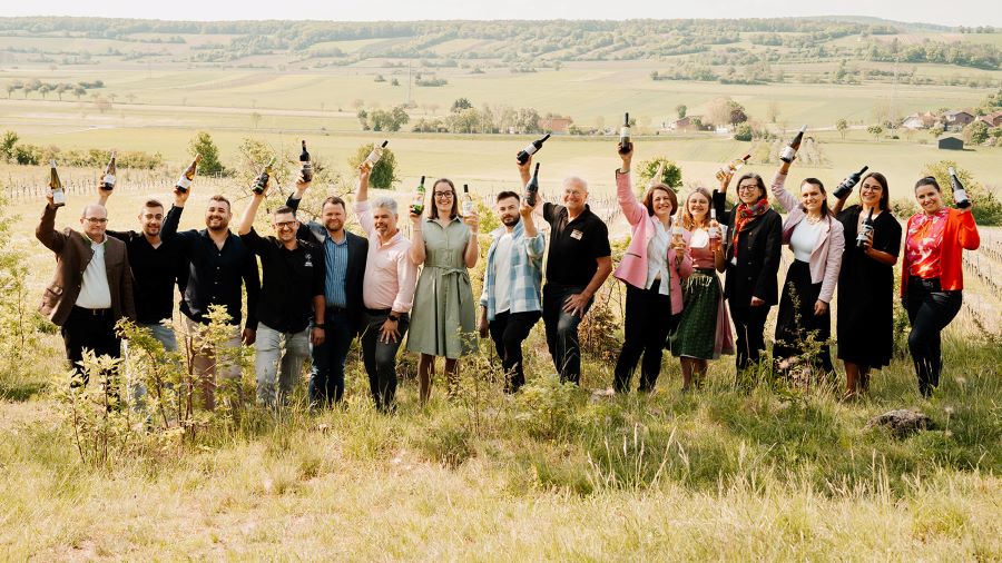 Eine Menschengruppe mit Weinflaschen posiert draußen für ein Pressefoto.