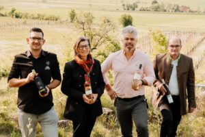 Vier Menschen halten je eine Weinflasche und lächeln in die Kamera.