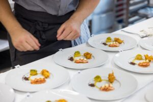 Teller mit angerichteten Speisen, dahinter steht ein Koch und begutachtet die Teller.