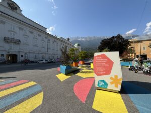 Installation Urban Blooms in Innsbruck. Bunte Bemalungen am Asphalt Boden und bunte Möbel zieren einen Platz.
