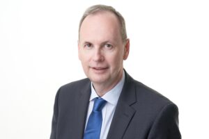 Portrait von Erich Moser. Er trägt einen schwarzen Anzug und eine blaue Krawatte.