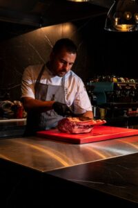 Präzision am Schneidebrett: Ein Koch portioniert ein großes Stück Fleisch in der offenen Küche.